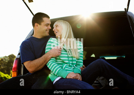 Couple s'amuser tout en étant assis sur le dos d'un camion dans un parking. Banque D'Images