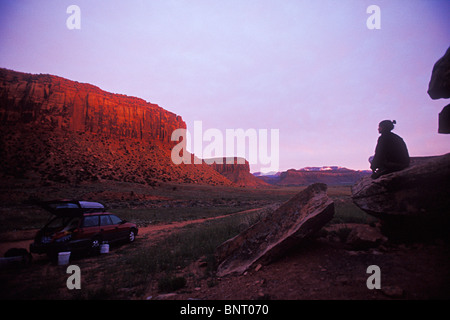 Femme assise sur un rocher soleil montres sur les falaises au-dessus de sa voiture. Banque D'Images