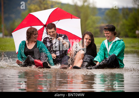 Quatre jeunes adultes rire alors qu'il était assis dans une grande flaque d'eau après un combat. Banque D'Images