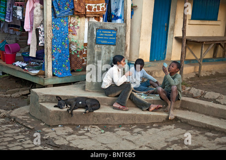 Trois enfants jouent aux cartes dans la rue à Andasibe Village de l'ouest de Madagascar. Un chien est en train de dormir sur l'étape à côté d'eux. Banque D'Images