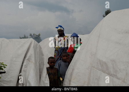 Les femmes congolaises déplacées se tiennent avec leurs enfants au milieu de cabanes de paille recouvertes de bâches en plastique contre la pluie dans un camp de déplacés improvisés au Nord-Kivu, RD Congo Afrique Banque D'Images