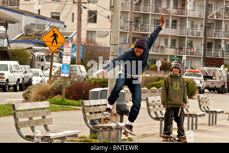 Cette jeune africaine est la planche à roulettes d'un banc de la ville alors que son ami asiatique est à proximité de regarder dans cette ville urbaine la vie. Banque D'Images