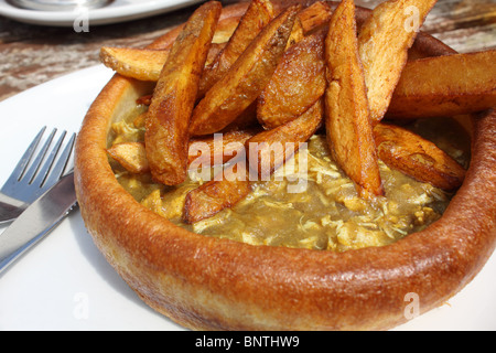 Yorkshire pudding géant, un repas traditionnel anglais, mais avec un remplissage de poulet au curry, servi avec des chips de pomme de terre Banque D'Images