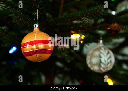 Un soufflé à la main d'ornement de Noël se bloque avec une bille de verre plus moderne sur une épinette de lumières colorées. Banque D'Images