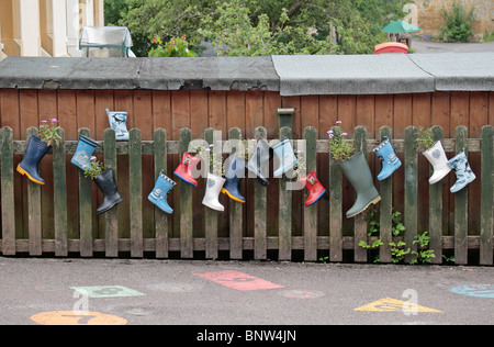 Un jardin coloré fabriqué à partir d'une rangée de bottes assorties sur une clôture dans la cour de l'école primaire. Symondsbury Banque D'Images