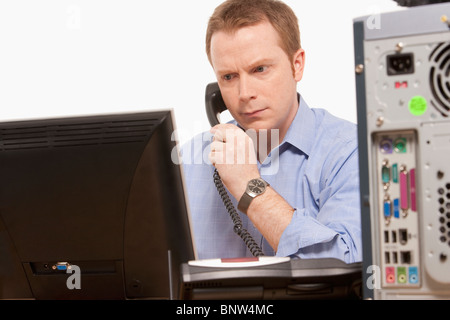 Businessman talking on phone while looking at computer Banque D'Images