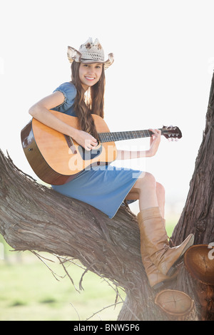 Cowgirl sitting in tree playing guitar Banque D'Images