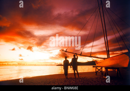 Couple debout à côté d'outrigger canoë sur Bora Bora shore holding hands sous ciel coucher de soleil spectaculaire Banque D'Images