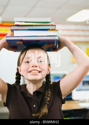 Elementary Student holding une pile de livres sur la tête. Banque D'Images