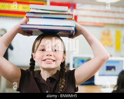 Elementary Student holding une pile de livres sur la tête. Banque D'Images