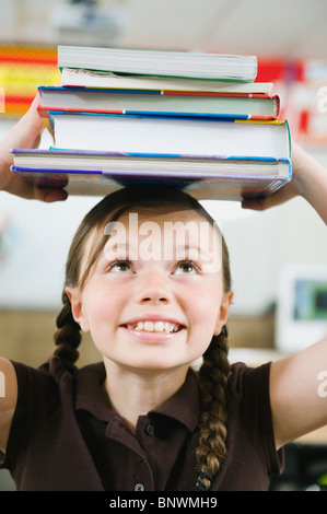 Elementary Student holding une pile de livres sur la tête. Banque D'Images