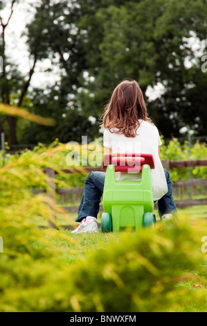 Jeune fille assise sur un vélo chariot en plastique dans un jardin Banque D'Images