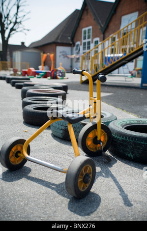 Un tricycle garé sur une aire de l'école vide sur une journée ensoleillée, avec pneus à jouer avec ainsi Banque D'Images