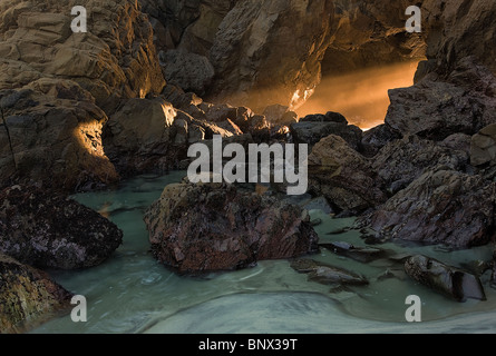 Un accueil chaleureux de l'arbre de lumière au coucher du soleil se déverse à travers un passage de la mer à marée basse, Pfeiffer Beach, côte de Big Sur, Californie, USA Banque D'Images