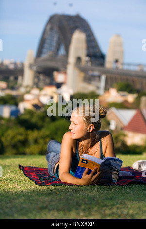 Un routard lit son guide en parc de l'Observatoire, surplombant le port de Sydney - Sydney, Nouvelle-Galles du Sud, Australie. Banque D'Images