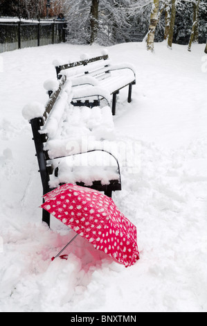 Un parapluie rouge dans la neige près d'un banc. Wrington, Somerset, Angleterre. Banque D'Images