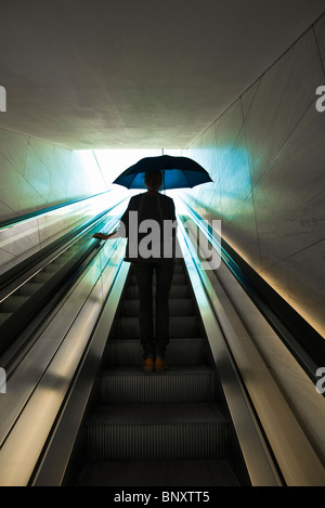 En montant l'escalator holding parapluie ouvert prêt à aller à l'extérieur Banque D'Images