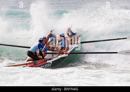 Un équipage de surfboat rowing à travers les vagues pendant une course à Cronulla Beach. Sydney, New South Wales, Australia Banque D'Images