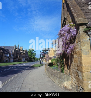 Village de Broadway High Street, Cotswolds, Worcestershire, Angleterre Royaume-uni avec mur de glycines en fleurs formés Banque D'Images