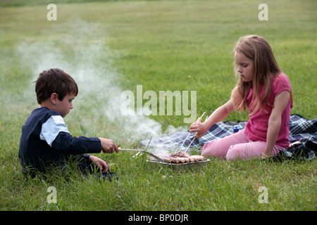 L'Angleterre, l'île de Wight. Cuisine Enfants saucisses sur un barbecue au camping, ferme Compton près de Brook sur la côte sud-ouest. (MR) Banque D'Images