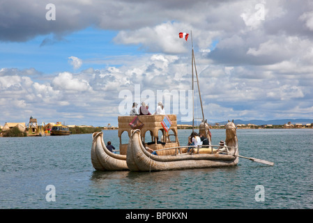 Le Pérou, un grand bateau de roseau est ramé vers le bas le chenal principal entre les îles flottantes des Uros sur le lac Titicaca. Banque D'Images