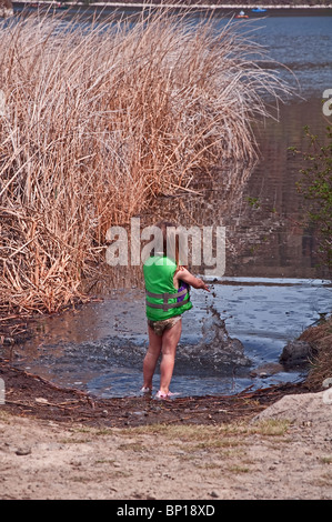 Cette jolie fille 3 ans de la petite enfance a beaucoup de plaisir à jouer dans la boue avec un puissant à la rive d'un lac Banque D'Images