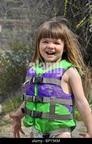 Cette jolie jeune fille de race blanche de 3 ans est souriant et heureux en jouant à l'extérieur. Elle porte un gilet vert et couverts. Banque D'Images