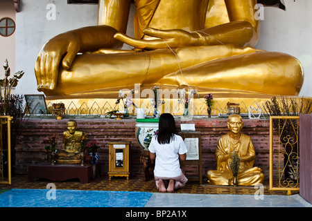 Une jeune femme thaïlandaise prie devant un Bouddha assis Banque D'Images