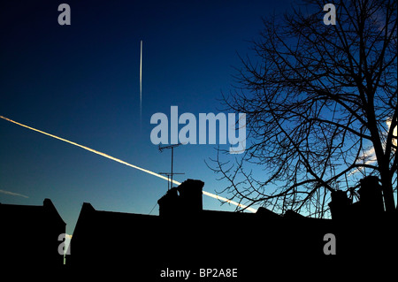 Des traînées de vapeur d'avion dans le ciel en fin de soirée, sur la silhouette du Victorian maisons dans la banlieue nord de Londres. Banque D'Images