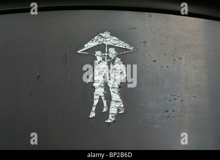 Graffiti sur un mur de métal gris à Londres, au Royaume-Uni, d'un homme et femme marche sous un parapluie Banque D'Images