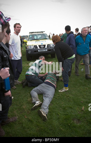 Homme étendu sur le sol en attente de soins médicaux après avoir été foulés au cours de jeu traditionnel de Bottlekicking, Leicestershire, UK Banque D'Images