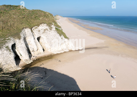 Couple en train de marcher sur la plage déserte à la Roche Blanche entre Portrush et Bushmills, Irlande du Nord. Falaises de calcaire érodé Banque D'Images