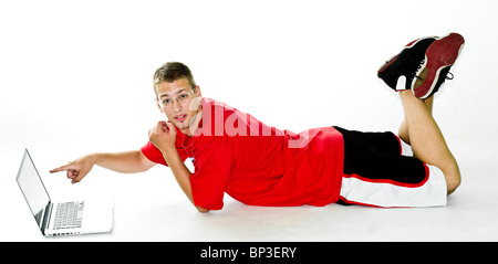 Jeune homme montrant quelque chose sur un ordinateur portable, tout en se trouvant sur le plancher dans le sport vêtements, isolé sur fond blanc Banque D'Images