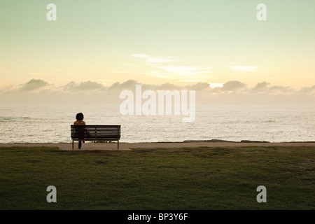 Femme assise sur un banc de parc en regardant Lever coucher de soleil sur l'océan Banque D'Images