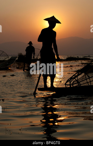 Les pêcheurs sur le lac Inle au Myanmar jeter leurs filets coniques dans l'eau comme le soleil se couche derrière eux. Banque D'Images