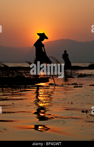 Les pêcheurs sur le lac Inle au Myanmar jeter leurs filets coniques dans l'eau comme le soleil se couche derrière eux. Banque D'Images