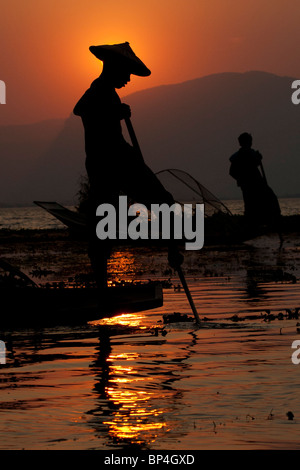 Les pêcheurs sur le lac Inle au Myanmar jeter leurs filets coniques dans l'eau comme le soleil se couche derrière eux. Banque D'Images