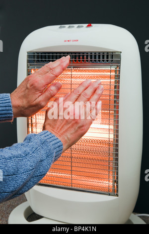 L'un des hauts femme essayant de se garder au chaud en le réchauffant les mains devant un appareil de chauffage halogène à faible consommation d'énergie en hiver. Angleterre Royaume-uni Grande-Bretagne Banque D'Images