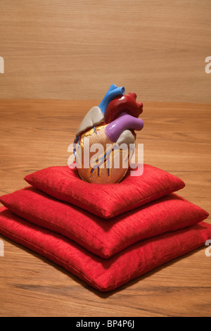 Modèle coeur en plastique sur la pile de coussins rouge Banque D'Images