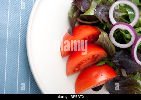 Salade sur assiette blanche avec des légumes verts, tomates et oignons rouges. Banque D'Images