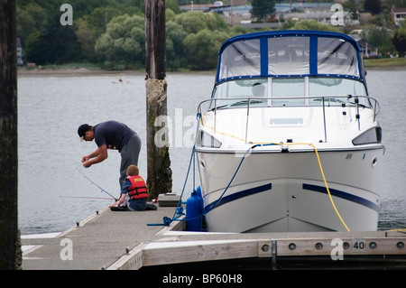 Un père aide son fils avec une ligne de pêche près de leur bateau à un quai à Miami, Washington. Banque D'Images