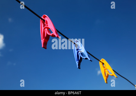 Trois pinces à linge colorées sur une ligne extérieure traditionnelle sur un ciel bleu clair. Banque D'Images
