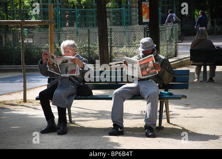 Les personnes lisant le journal sur le banc de parc parisien France Banque D'Images