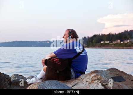 Heureux détendue homme assis sur des roches à bord de l'eau au coucher du soleil est une étude de contentement face à Puget Sound Edmonds WA Banque D'Images