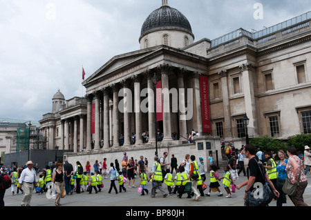 Un groupe d'enfants de l'école sur une sortie traverser Trafalgar Square à Londres wearing high-vis jackets Banque D'Images