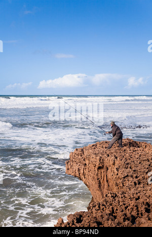 Pêcheur utilisant la tige traditionnelle et la ligne sur les falaises accidentées, Plage Aglou, Tiznit, côte Atlantique, Maroc Banque D'Images