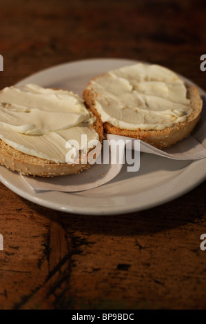 Un bagel sésame grillées est servi avec fromage à la crème sur une assiette blanche. Banque D'Images