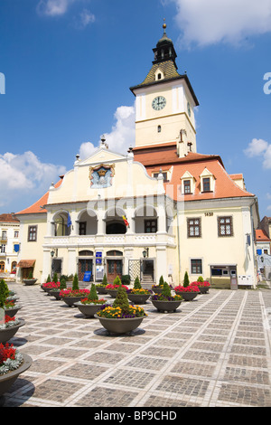 Un bâtiment historique de l'hôtel de ville avec une tour de l'horloge proéminente et un toit de tuiles rouges se dresse sur une place publique pavée sous un ciel bleu vif avec des nuages dispersés. Le bâtiment dispose d'une couleur crème Banque D'Images