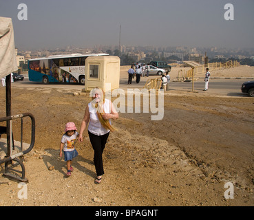 Dame anglaise'avec demi-Thai girl à pied vers les pyramides de Gizeh en Egypte avec Le Caire sur l'horizon et la barrière de sécurité Banque D'Images