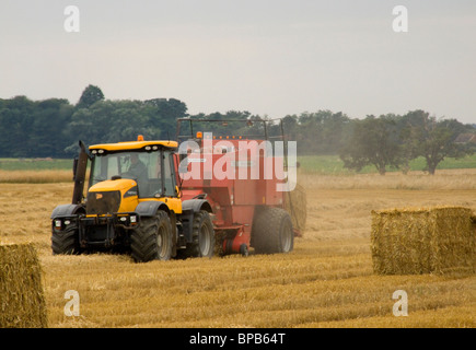 JCB 4x4 tracteur Massey Ferguson 190 avec joint de la ramasseuse-presse travaillant dans un champ avec une balle dans le champ et qu'un sur le point d'être éjecté Banque D'Images